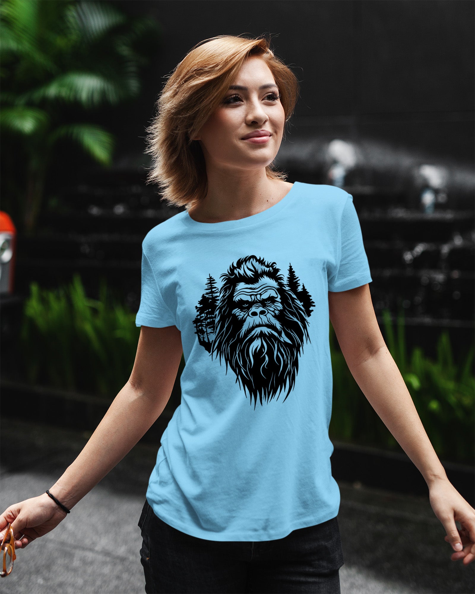 Person wearing a t-shirt featuring a stylized Bigfoot face with pine trees forming part of the wilderness design.