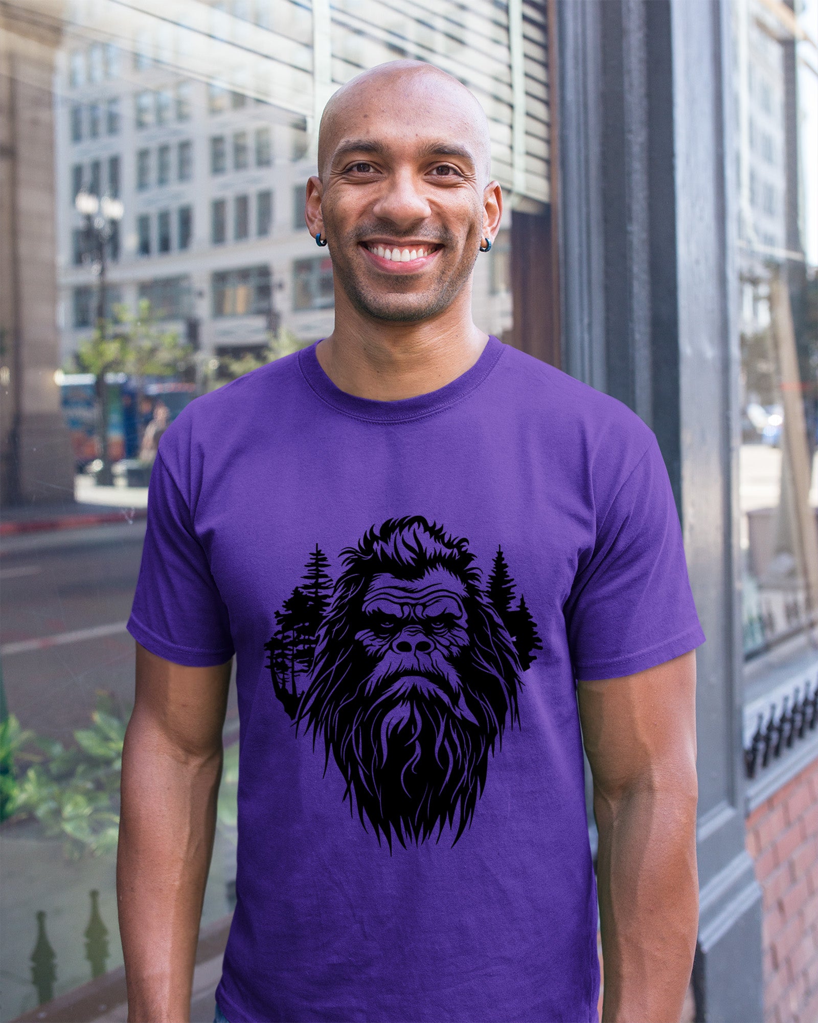 Person wearing a t-shirt featuring a stylized Bigfoot face with pine trees forming part of the wilderness design.